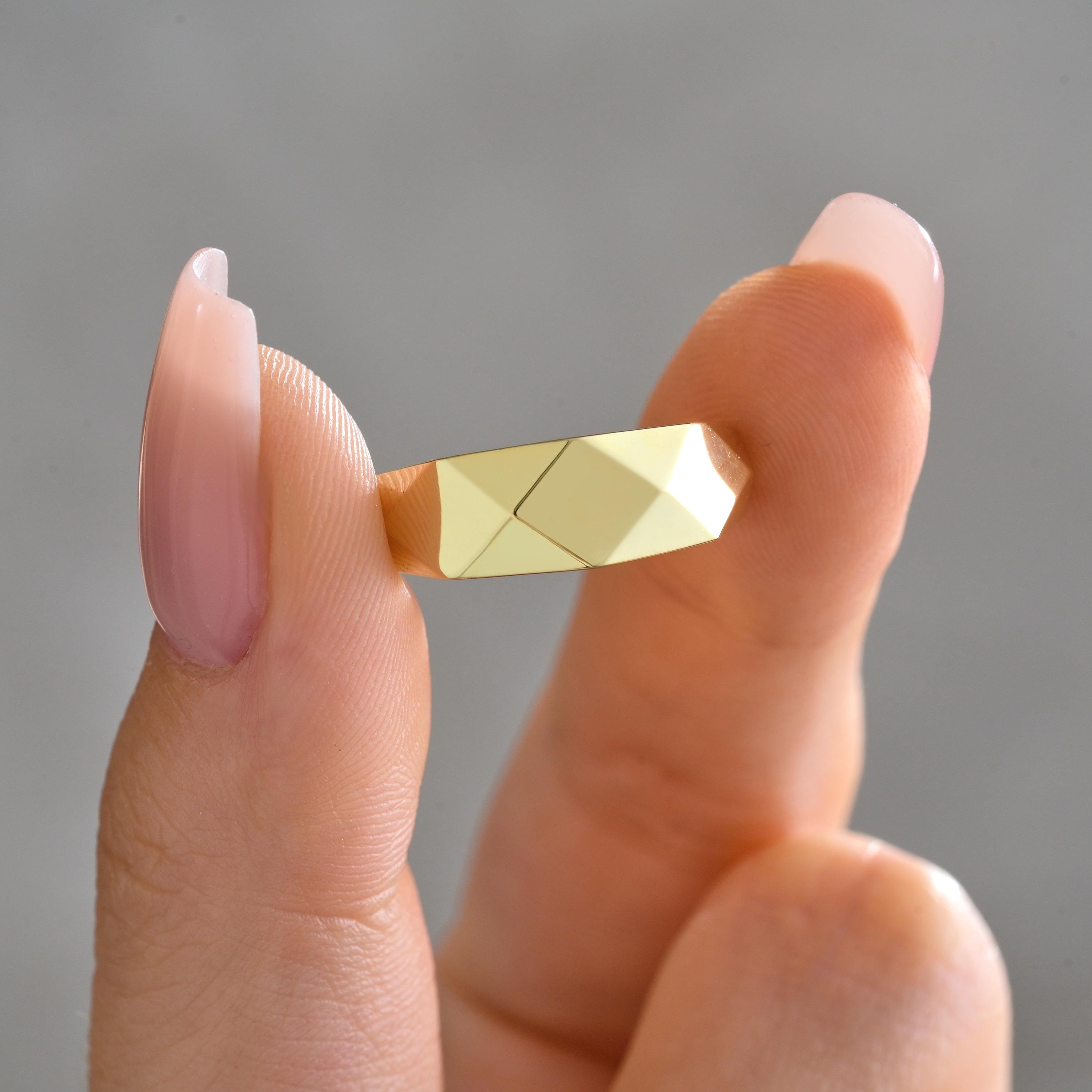 faceted gold ring held between fingers highlighting angular geometric cuts