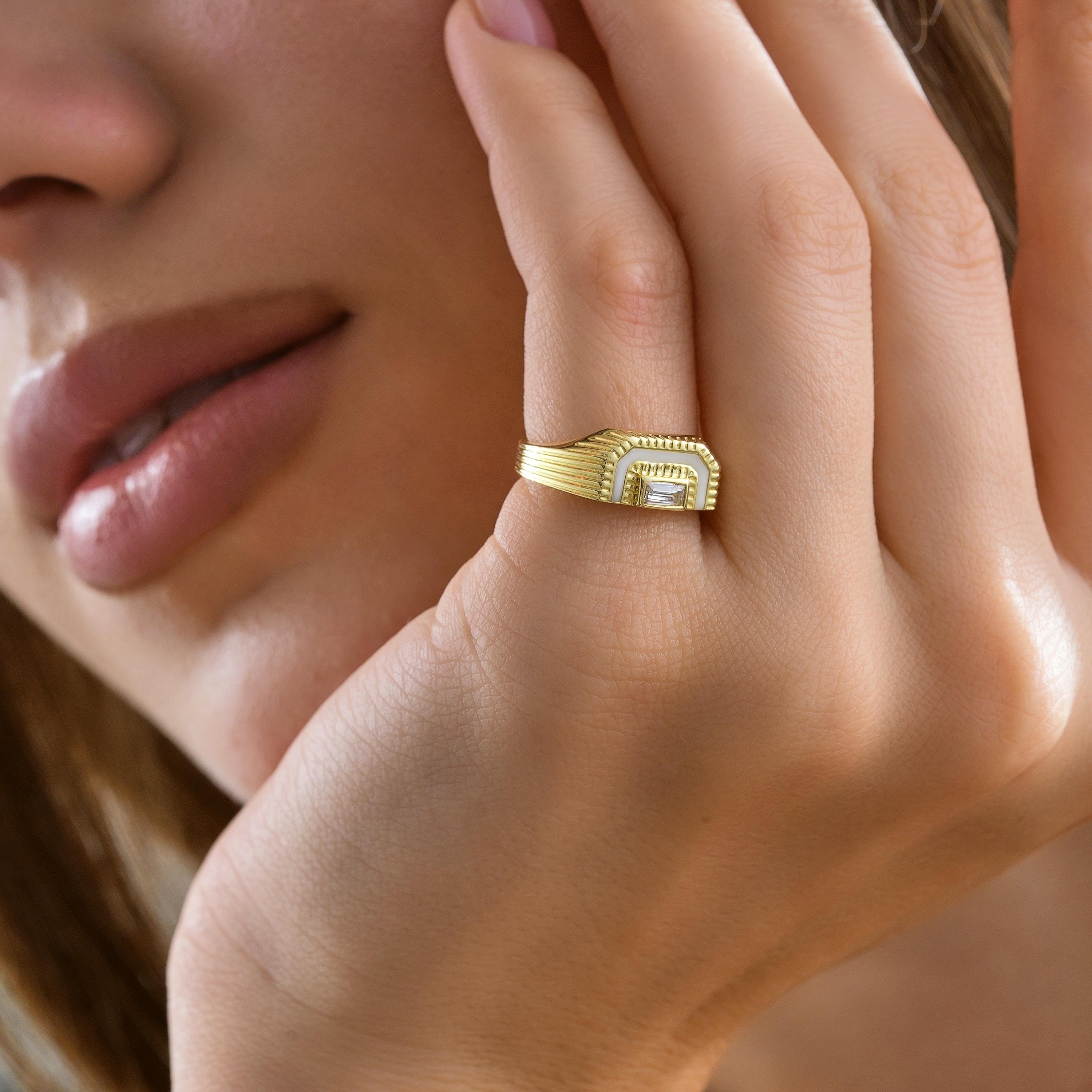 Model hand pinky finger shot showing ribbed fluted shoulders on a gold signet ring with white enamel inlay and baguette CZ diamond