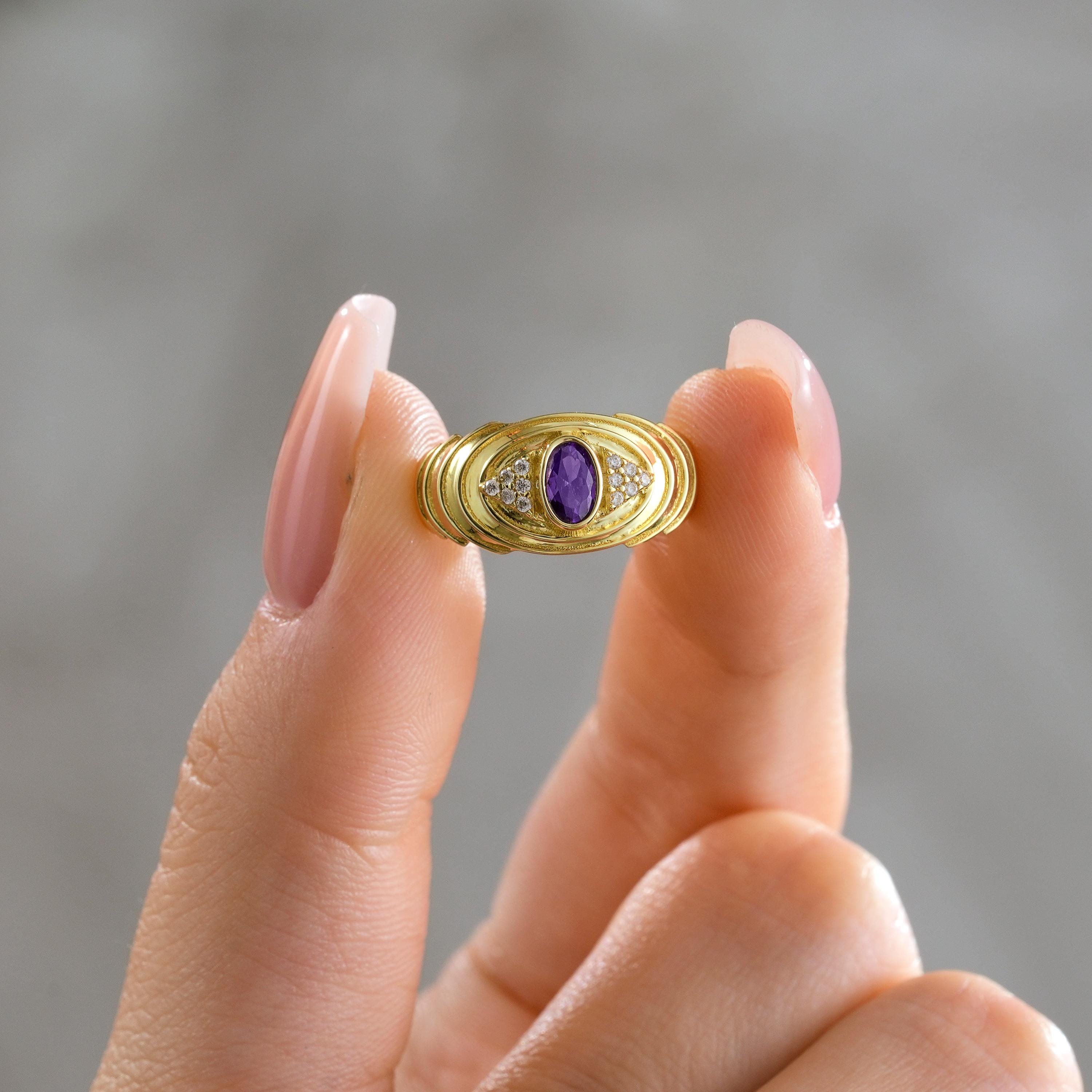 hand holding solid gold ripple shank ring with bezel set oval purple stone and round pavé details