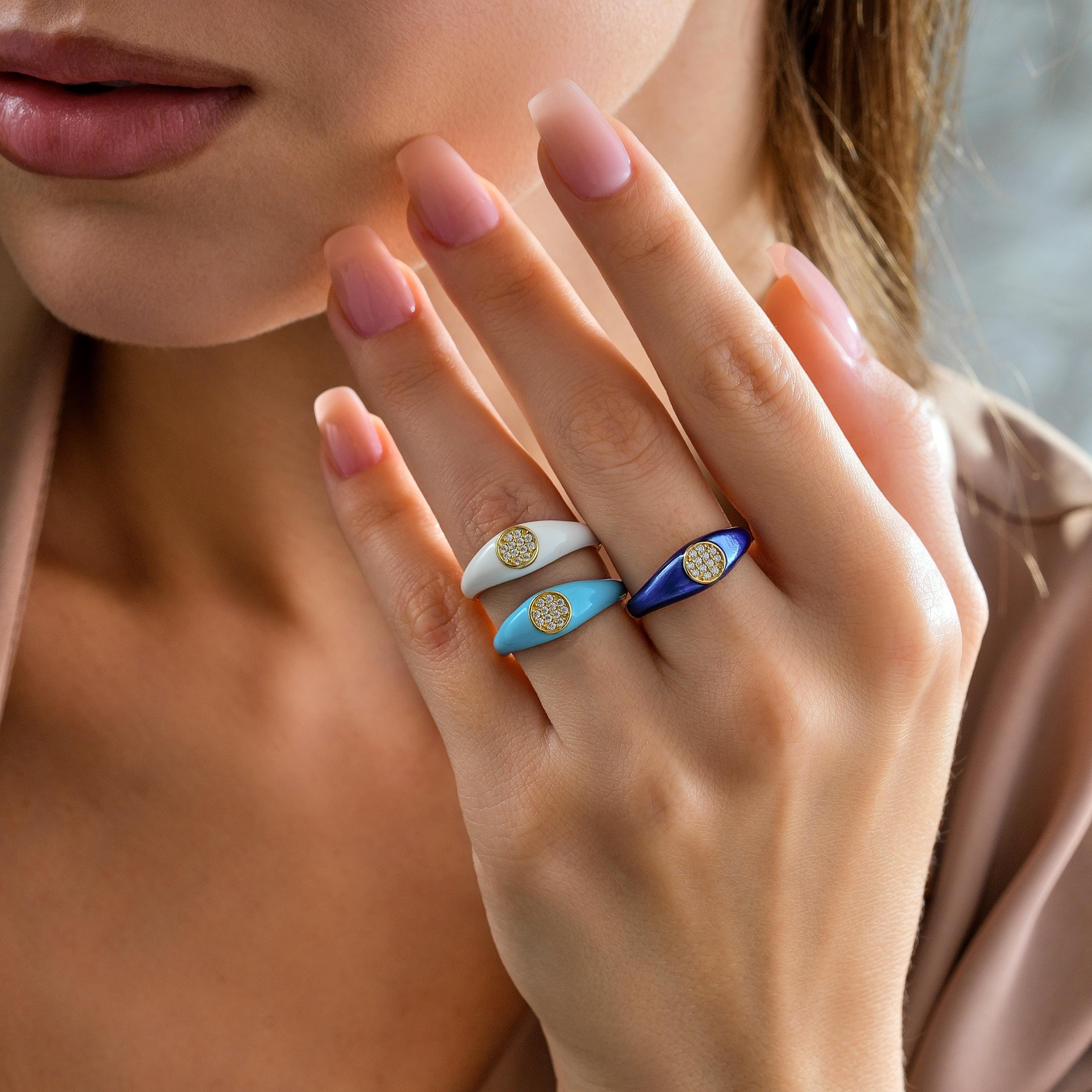 Three enamel solid gold signet rings in turquoise, white, and deep blue enamel with round pave discs displayed on hand