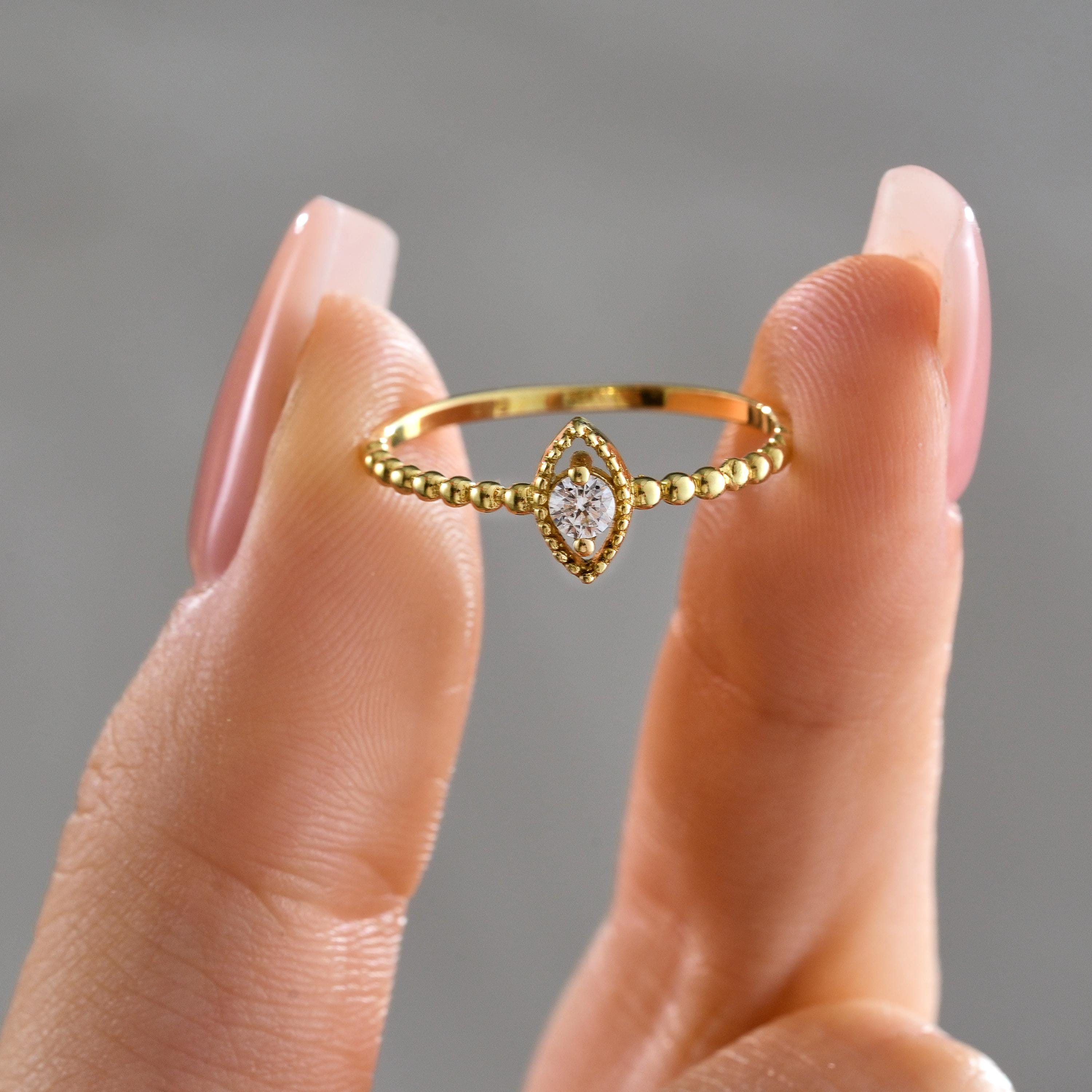 A dainty solid gold ring with a marquise centerpiece and beaded band held between fingers, showcasing the round CZ center stone
