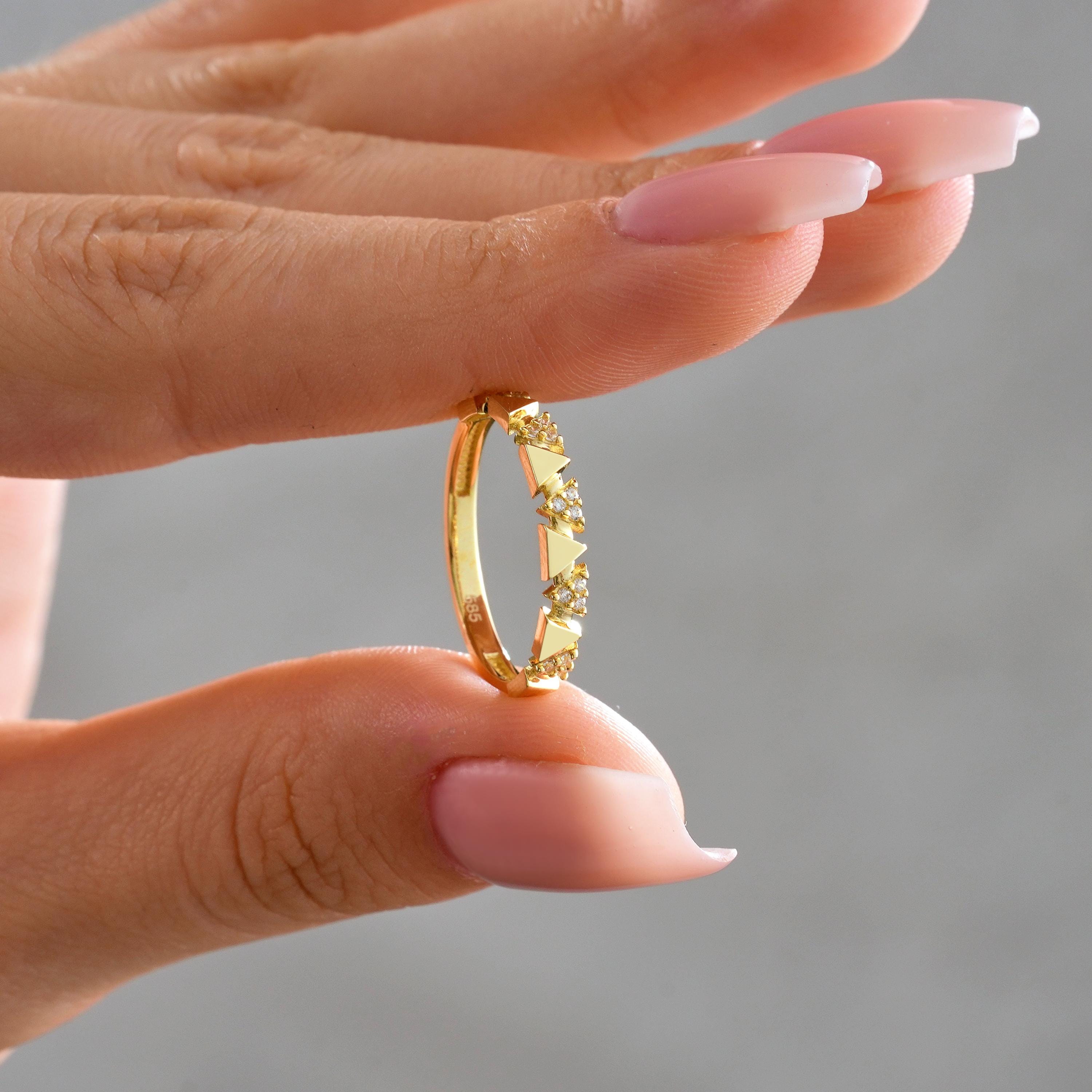 Solid gold triangle band ring with round CZ stones held between fingers, showing geometric triangle accents