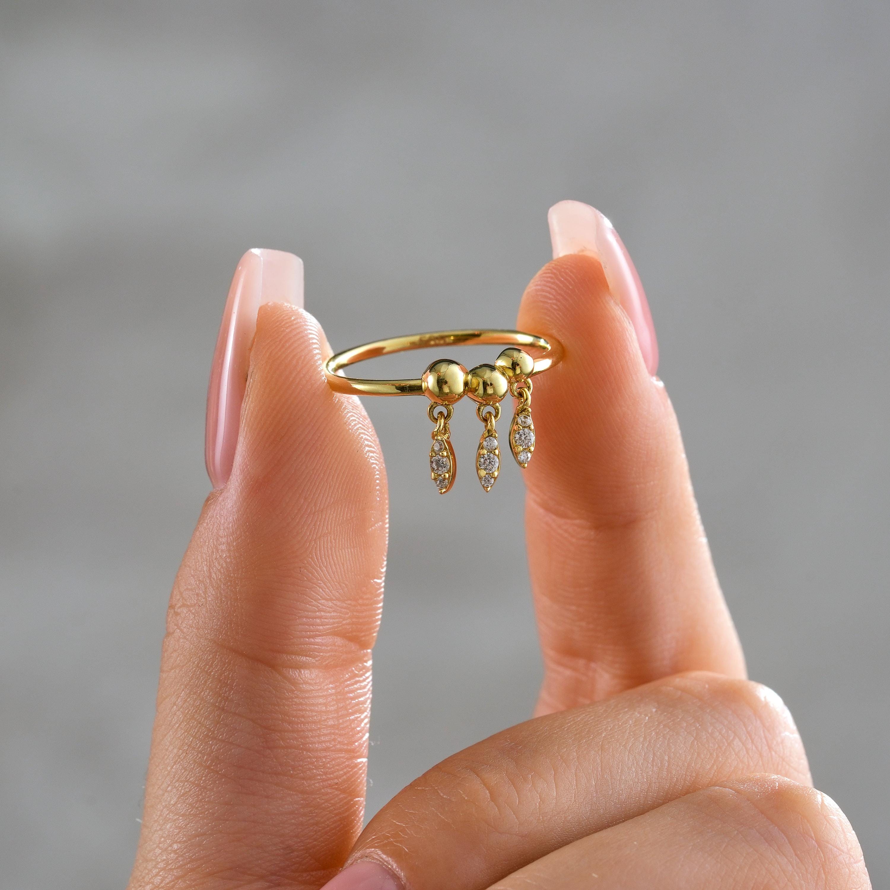 solid gold ring with three polished bead tops and dangling CZ diamond teardrop charms shown between fingers