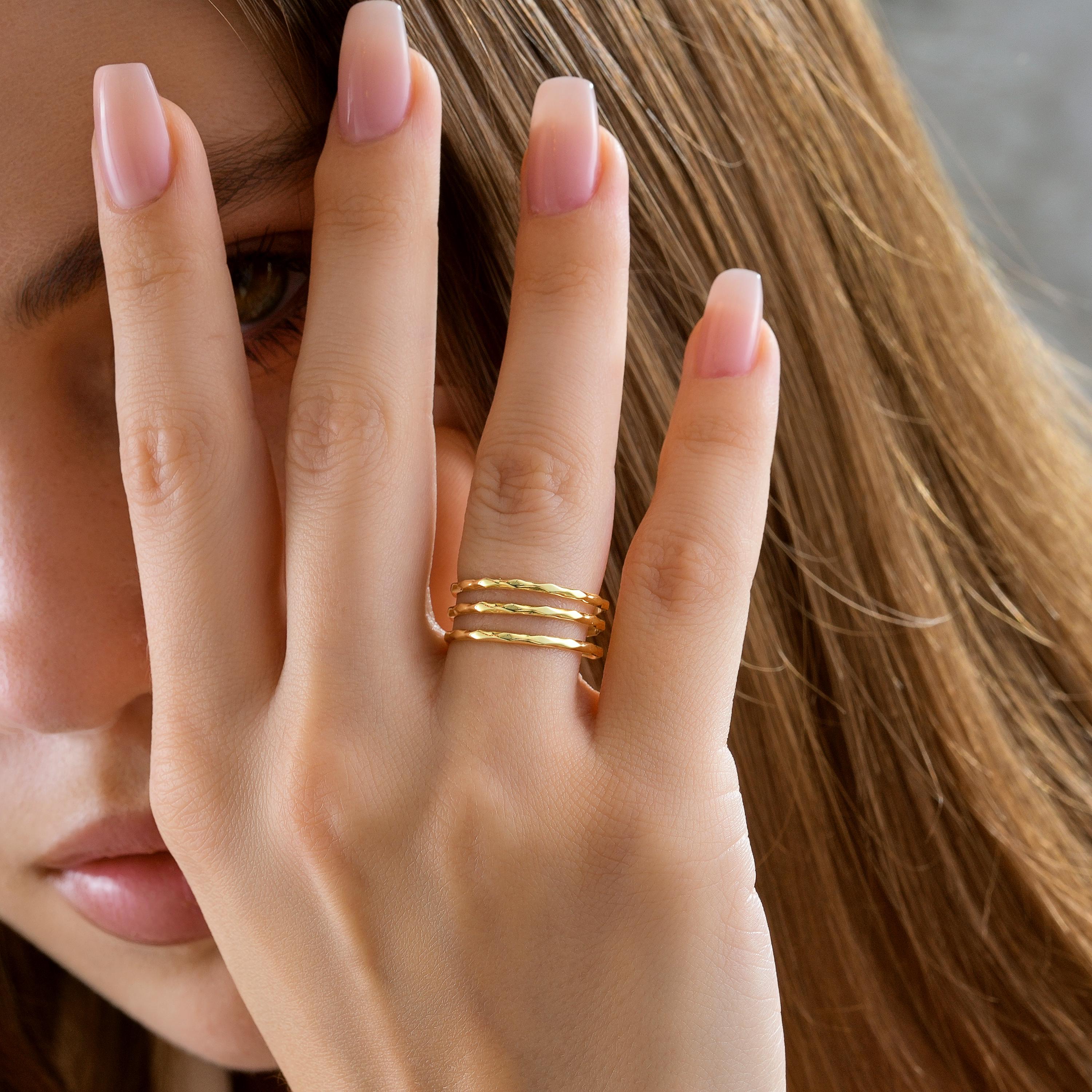A minimalist solid gold ring featuring a triple row stacked design with an organic hammered texture