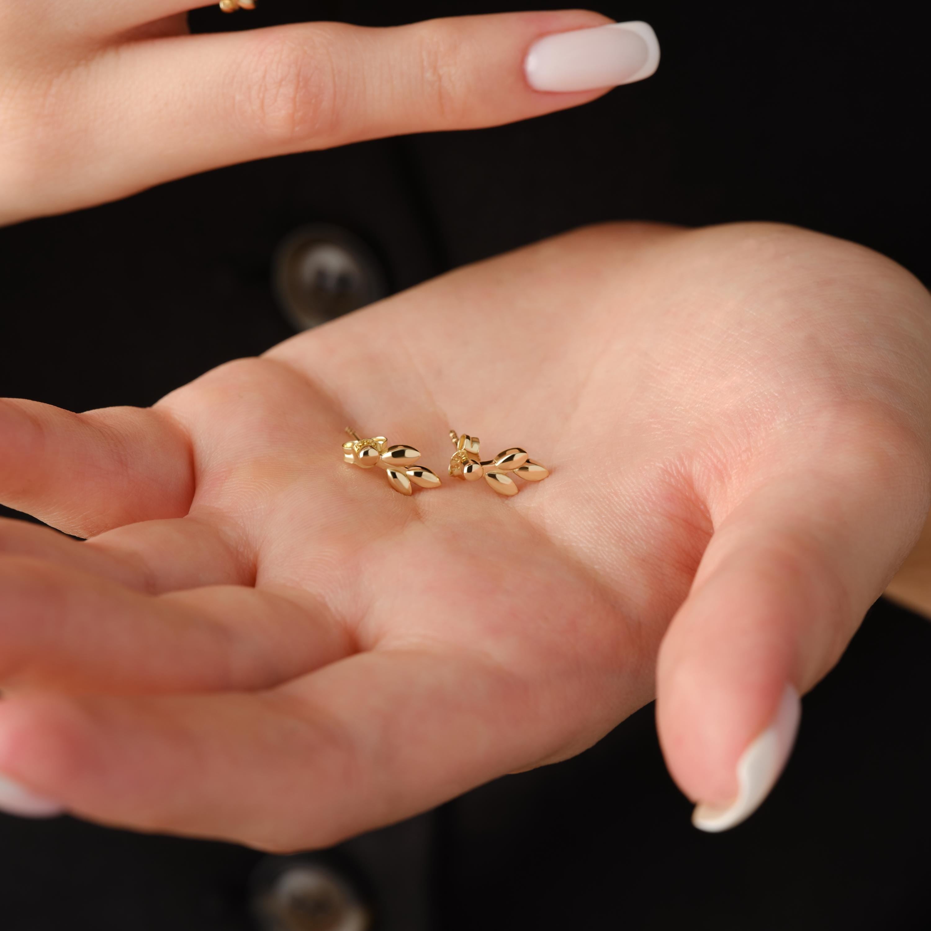 Pair of leaf gold studs shown in hand.