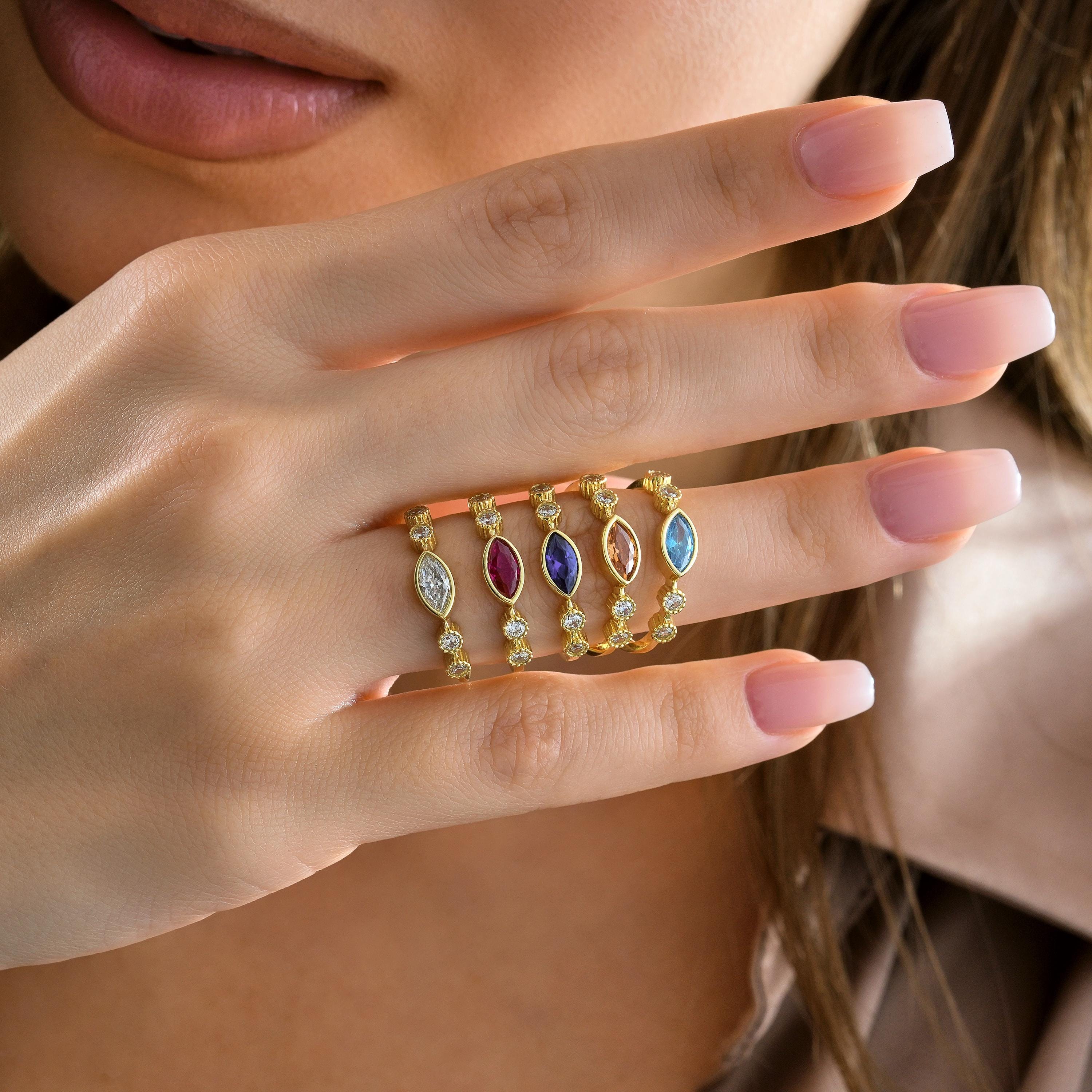 five bezel set gold marquise rings in multiple stone colors including sapphire, ruby, clear white diamond, pink, and aquamarine