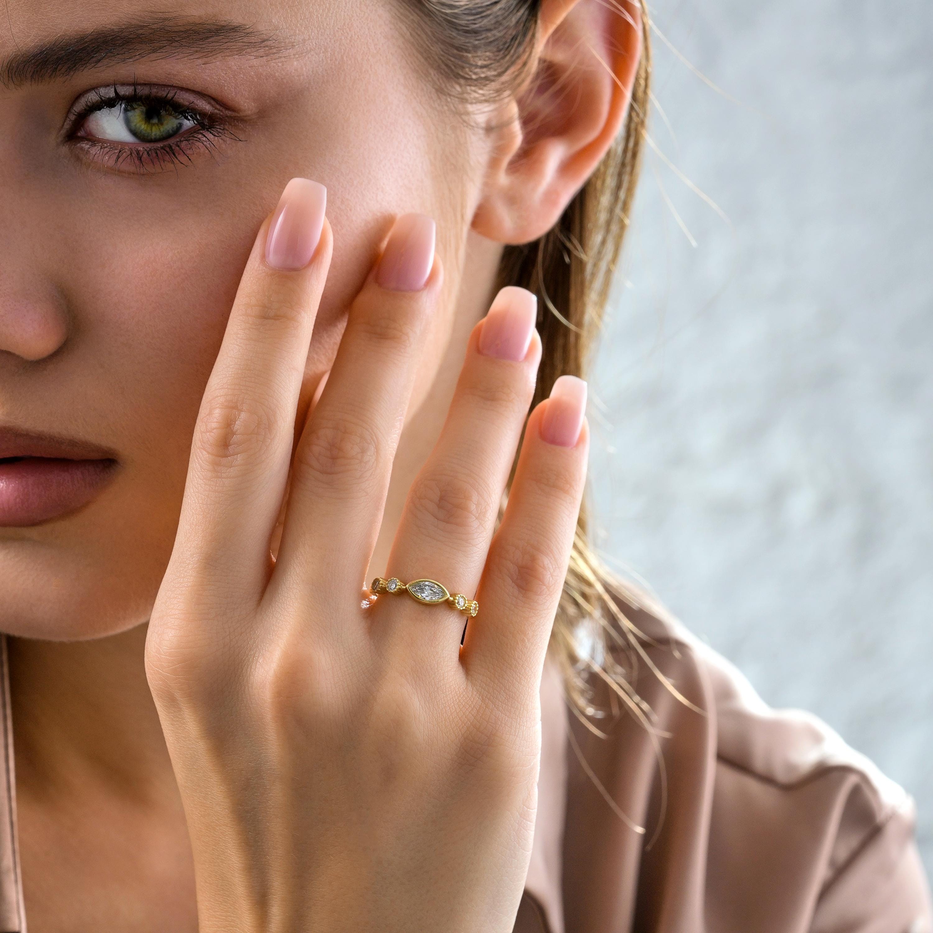 woman wearing marquise bezel solid gold ring near face, showcasing dainty band and round brilliant stones