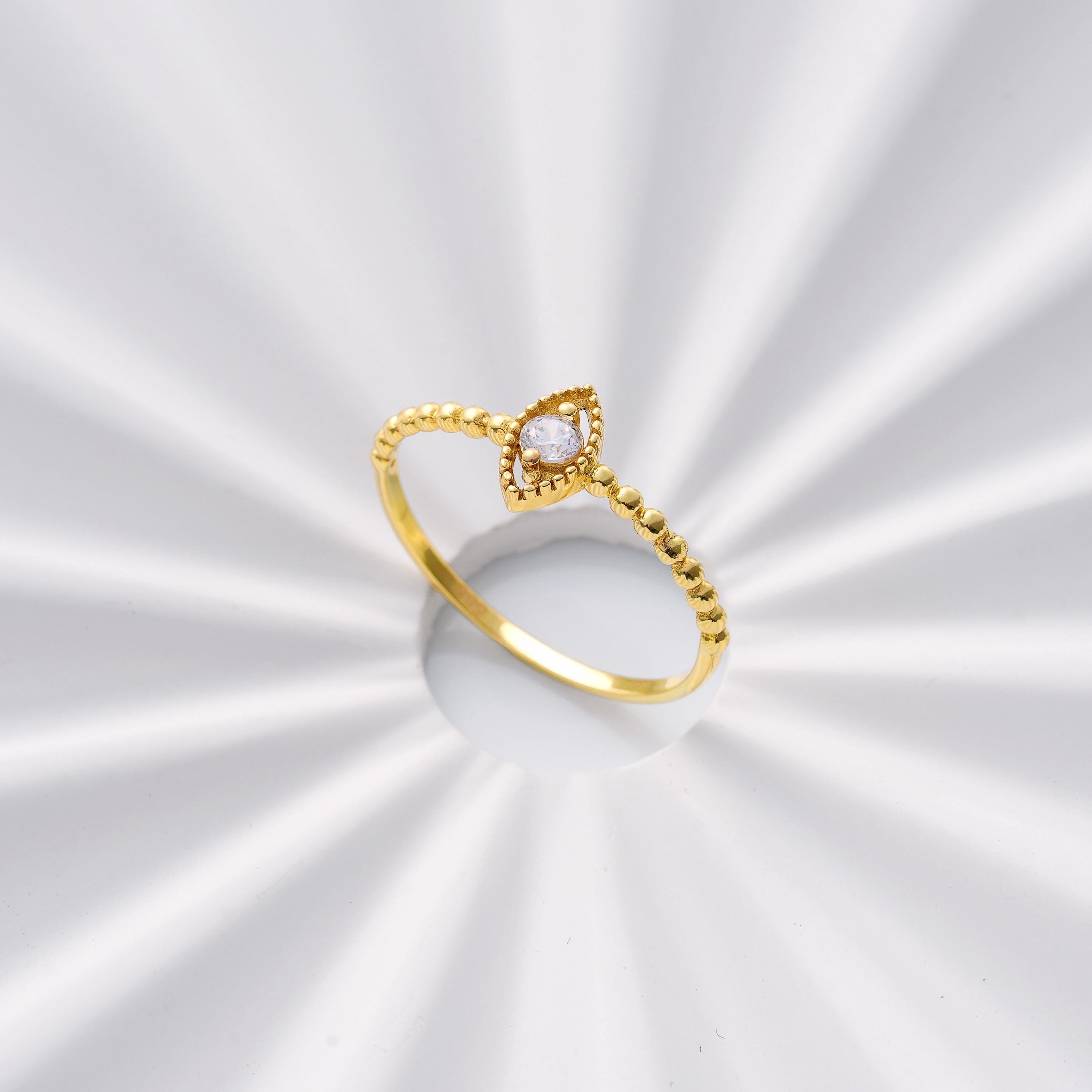 dainty solid gold marquise shape band round CZ ring displayed on a reflective white surface with a beaded shank and delicate halo design