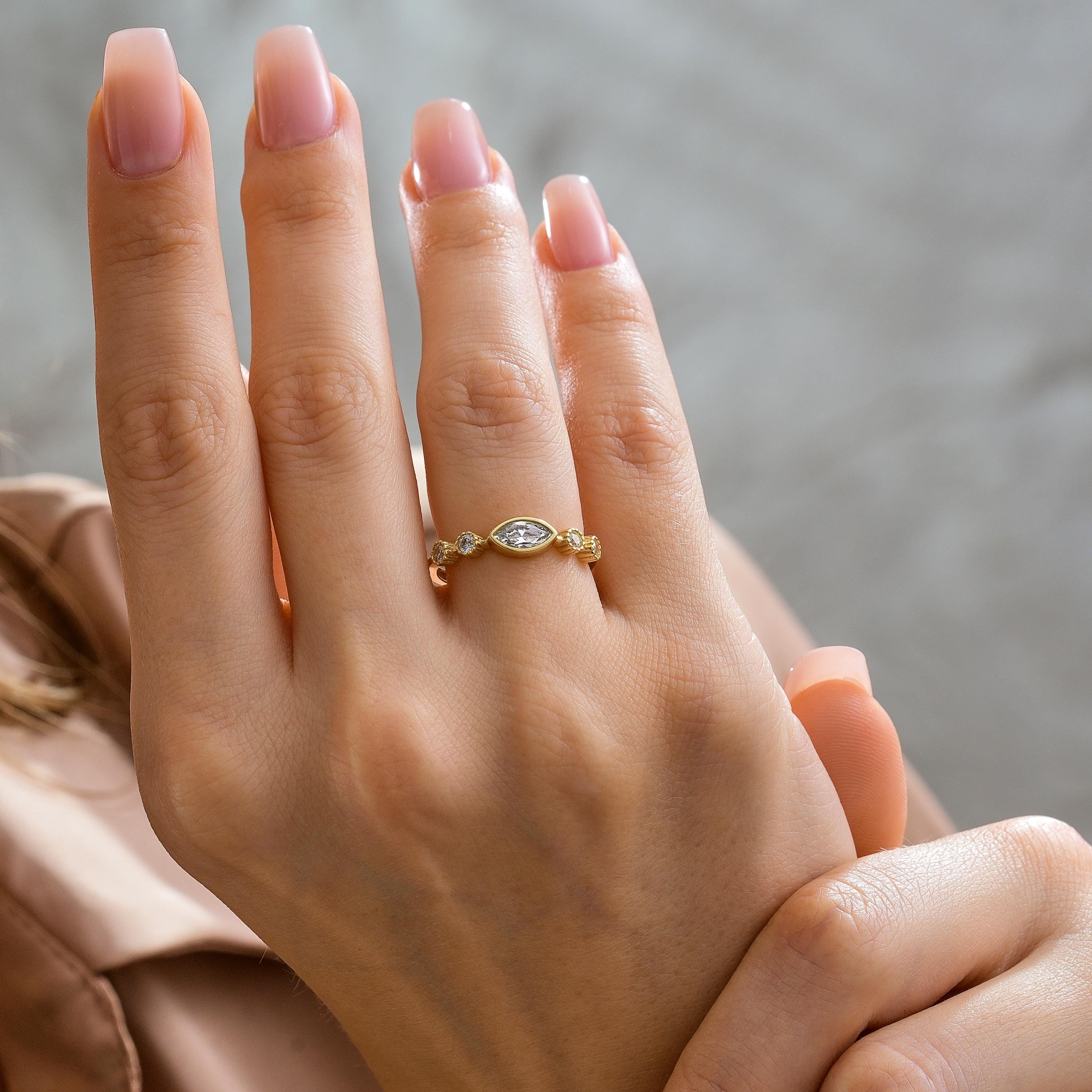 women wearing solid gold marquise bezel ring with white center stone and round diamond accents