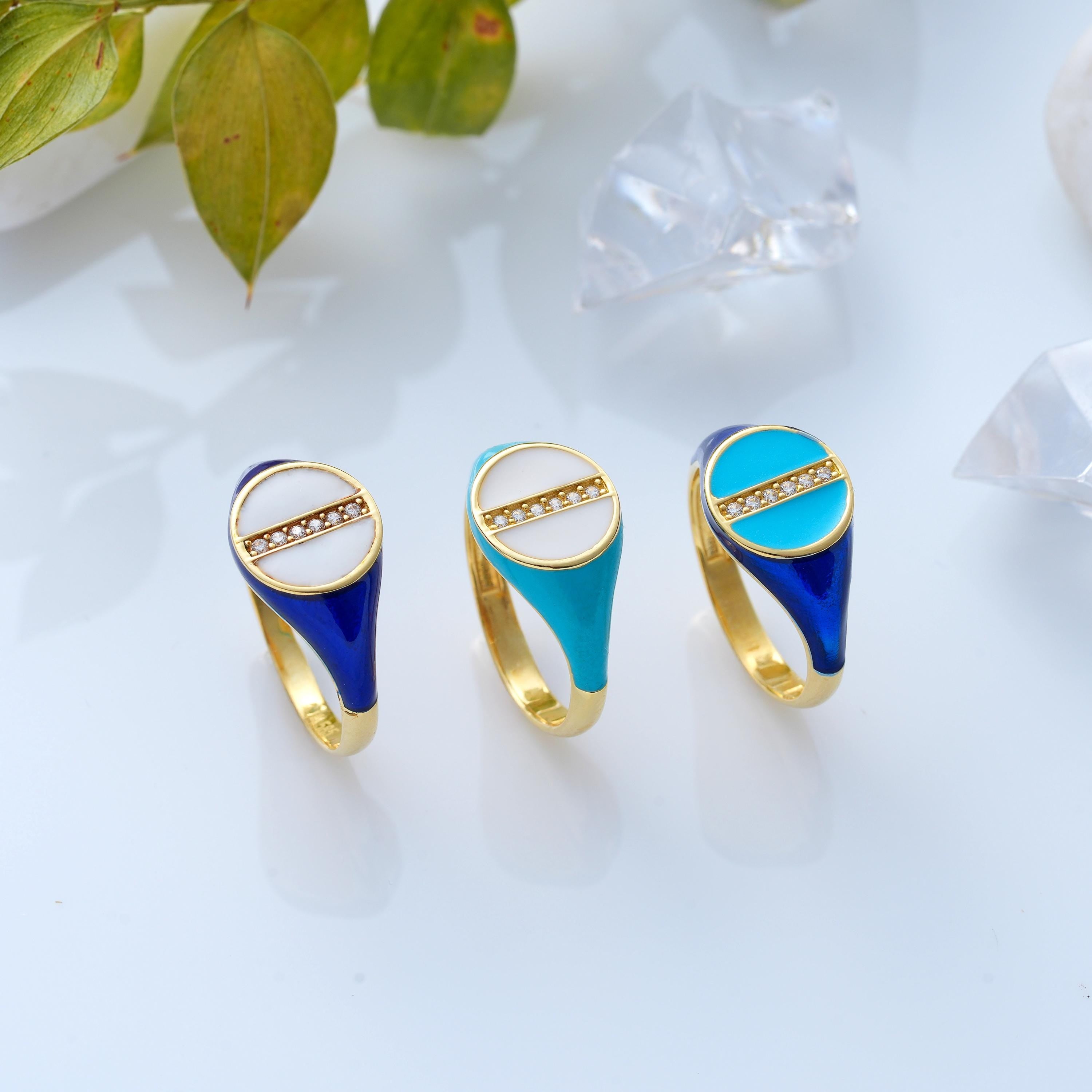 three circular enamel custom signet rings in different enamel colors: turquoise, white, and navy