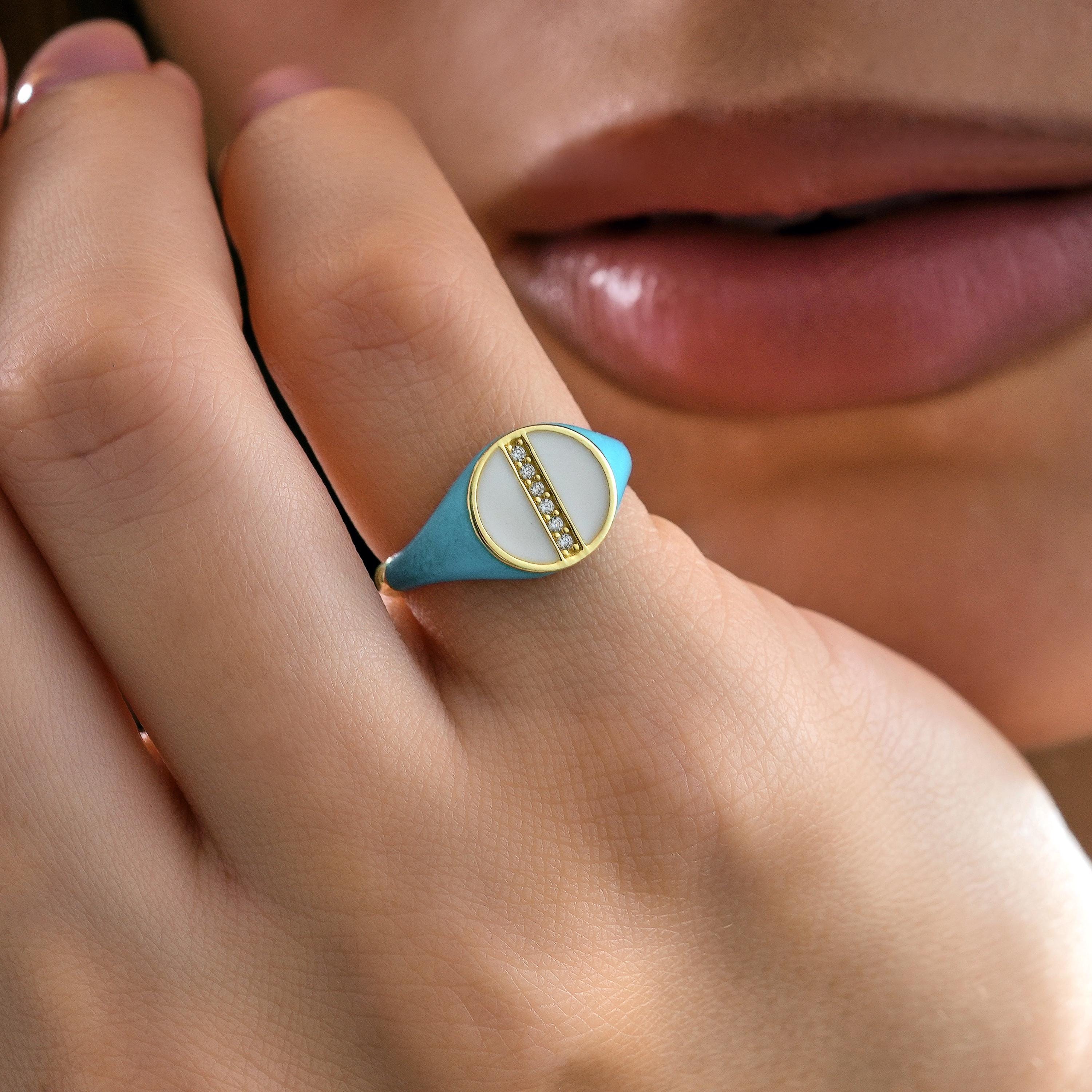 Woman wearing solid gold round signet ring with turquoise enamel band and white enamel circular top featuring pave diamond bar